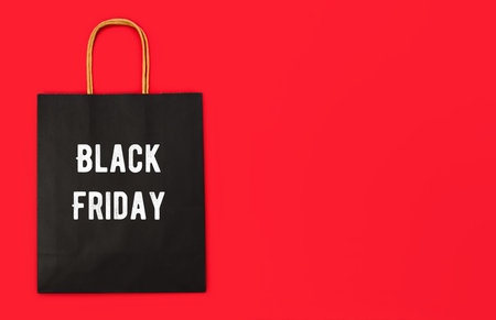 Paper black shopping bag with inscription Black Friday on the red background with copy space.