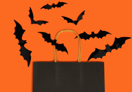 Paper black package and bats on orange background. Halloween shopping and sale concept. Flatlay. Top view. Copy space. Selective focus.の写真素材