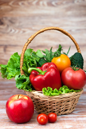 Fresh vegetables and greens in a wicker basket on a wooden table.の写真素材