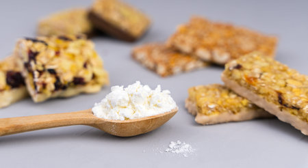 Whey protein powder in spoon and different energy protein bars on gray background. Close-up....