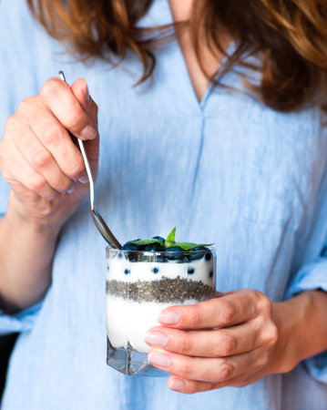 Young woman holding a glass of dessert with fresh blueberry, yogurt and chia seeds in her hands. Healthy breakfast concept. ?lose-up.の写真素材