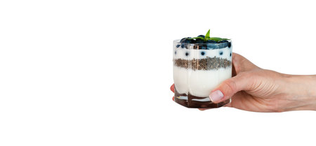 Woman's hand holds a glass of dessert with yogurt, fresh blueberry and chia seeds isolated on white background. Delicious and healthy breakfast. Banner. Copy space.の写真素材