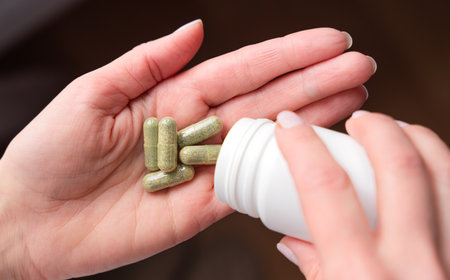 Women's hand pouring herbal pills from a bottle in her hand. Vitamins, bio supplement. Close-up. Selective focus.の写真素材