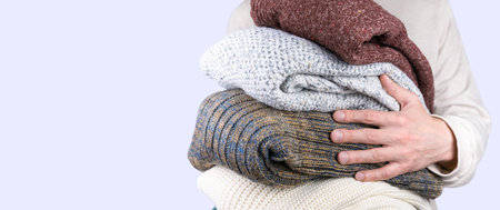 A young man holds warm knitted sweaters in her hands. Warm winter and autumn clothes. Copy space....