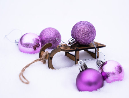 Winter festive composition with Christmas tree decorations and decorative small sledge on the snow. Close-up. Selective focus.の写真素材
