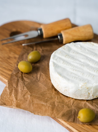 Camembert cheese, olives and knives for cutting on a wooden board. Close-up. Selective focus.