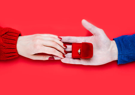 Man making marriage proposal. Male hand giving a gift box with engagement ring on red background....