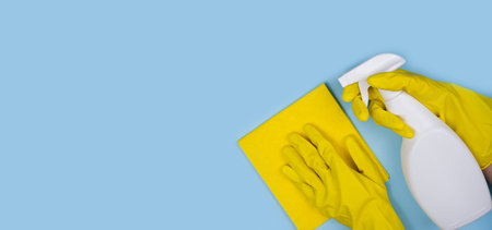 Banner. Woman's hands in yellow rubber gloves hold a cleaner spray and rag on a blue background....