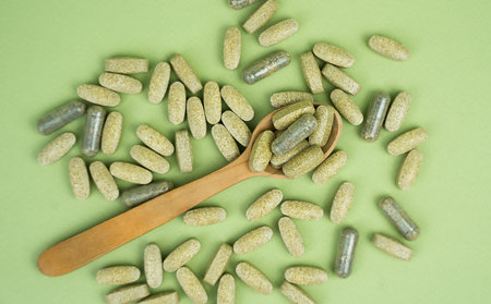 Natural supplements in a wooden spoon on a green background. Top view. Close-up.