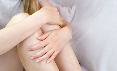 Young woman hugged her knees sitting on the bed. Depression, stress, pain, health problems....