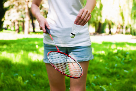 Young woman in white t-shirt and denim shorts playing badminton in the park in sunny day. Healthy lifestyle concept. Fitness concept.の写真素材