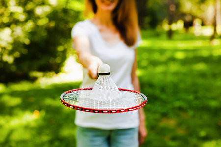 Young woman in white t-shirt and denim shorts holding shuttlecock and racket for badminton play in...