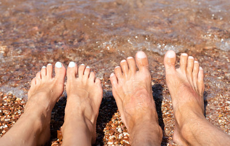 Woman's and man's feet on the beach by the sea. Rest and relaxation on the beach. Family vacation concept and travel. Close-up.の写真素材