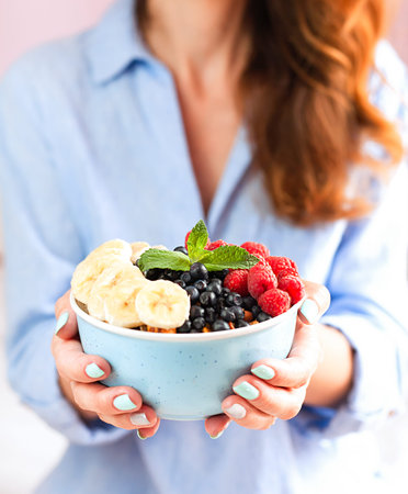 Smiling girl holding a bowl with muesli and fresh berries and fruits in her hands. Healthy breakfast...