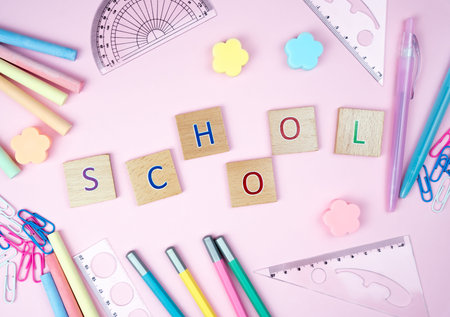 The letters Schooland school stationery lie on a pink background in the form of a frame. Top view. Back to school.の写真素材