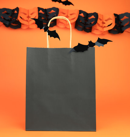 Paper black bag and decor for Halloween on orange background. Halloween shopping concept. Mock up. Copy space. Selective focus.の写真素材