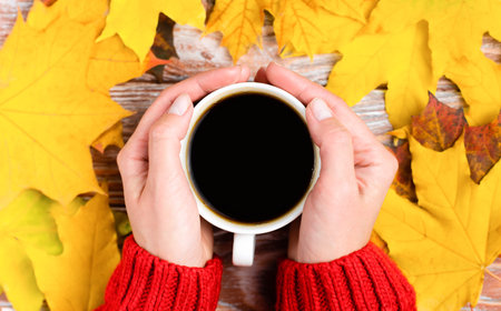 Autumn composition with woman's hands, cup of hot aromatic coffee and autumn yellow leaves. Flatlay....