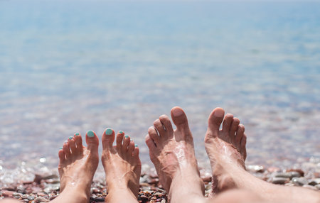 Legs of young man and woman on the beach by the sea. Enjoying the sun on a summer sunny day at the sea. Family vacation concept and travel. Close-up. Copy space.の写真素材