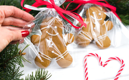 DIY gifts for Christmas. Woman's hand holding packed gingerbread man on a white wooden background....