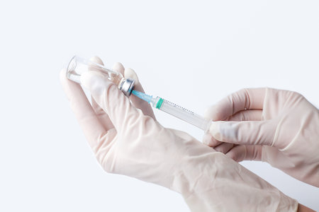 Doctor's or nur's hand in white protective gloves hold syringe with preparation for injection on the white background. Influenza and coronavirus vaccination. Close-up. Copy space.の写真素材