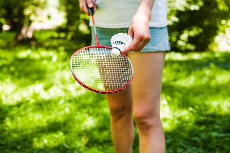 Young woman in white t-shirt and denim shorts playing badminton in the park in sunny day. Healthy lifestyle concept. Fitness concept.の写真素材