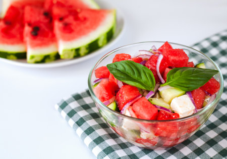 Fresh delicious juicy dietary salad with watermelon, feta cheese, cucumber, red onions and basil leaves on the plate. Close-up. Top view. Healthy food concept.の写真素材