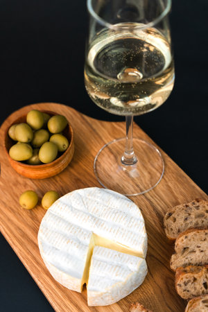 Camembert cheese, crispy baguette, olives and wineglass of white wine on a dark background. Close-up. Selective focus.の写真素材