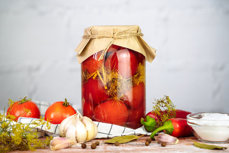 Delicious pickled homemade tomatoes in jar on a wooden background. Traditional autumn food storage. Organic farm vegetables in marinade. Close-up.の写真素材