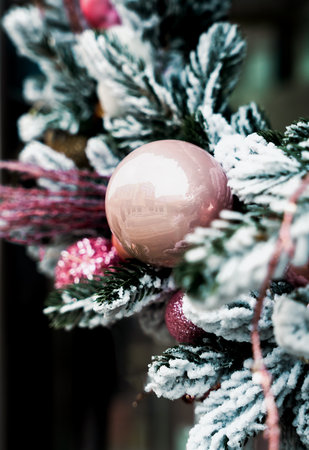 Elegant Christmas pink ornament on snow covered evergreen branches with a soft winter atmosphere. Close-up. Selective focus.の写真素材