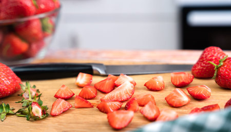 Slices of strawberries and a knife on the table at the kitchen. Preparing dessert or lemonade with fresh strawberries. Selective focus.の写真素材