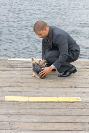 Ethnic Business Man with his Yorkshire Terrier Dog standing on a pier next to the lake.の写真素材