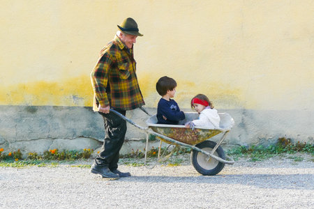 Italy October 29 2011 in the Tuscan hills during the afternoon an elderly gentleman carries two children with a wheelbarrowのeditorial素材