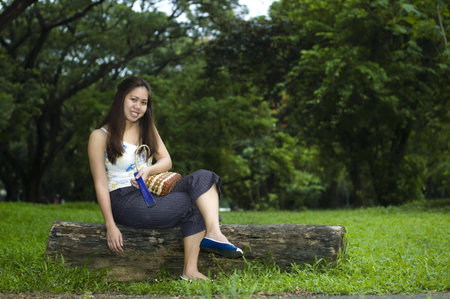 Smiling woman sitting on a log with lush foilage behind herの写真素材