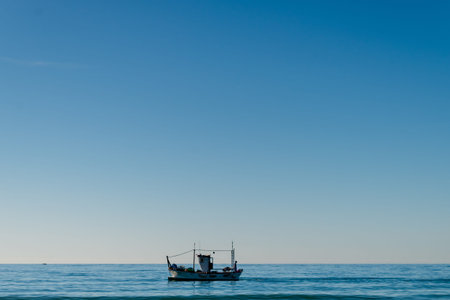 A lone fishing boat floats peacefully on the calm blue sea under a clear sky embodying tranquility...