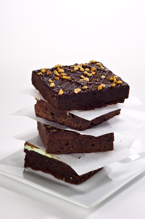 Four beautifully stacked gourmet brownies stacked on a white plate with parchment paper between each brownie.の写真素材