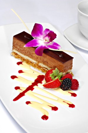 Beautifully plated chocolate mousse cake garnished with a purple orchid, strawberry, backberry and raspberry.  A zig zag of white chocolate and strawberry sauce completes the plate.の写真素材