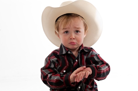 Portrait of a sad little boy in a cowboy hat. He is frowning and holding one hand in his other.の写真素材