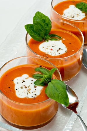 Small glass bowls filled with tomato soup along side sliver spoons.の写真素材