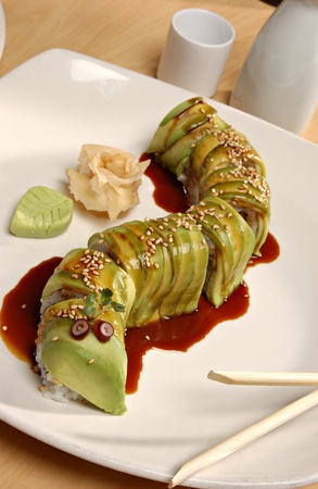 Japanese Avocado Roll (or Caterpillar Roll) with Eel Sauce on a white plate.  There is a rose made of ginger and a leaf made of wasabi on the side.  Chopsticks and a saki set in the background.の写真素材