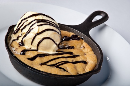 Skillet Baked Chocolate Chip Cookie dessert topped with ice cream and chocolate sauce drizzled.の写真素材