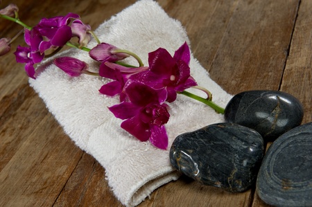 Vibrant pick orchid lays on a spa towel next to black stones. の写真素材