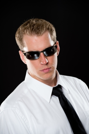 Portrait of a young male model wearing a white shirt, black necktie and dark sunglasses. Shot on a black background, using high-key lighting.の写真素材