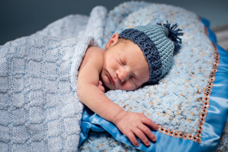 Newborn boy asleep on soft blue blankets, wearing a blue knit hat.