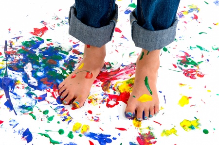 A young girl's feet covered in colorful paint on a paint splashed background.  She has her jeans rolled up to avoid the mess.の写真素材