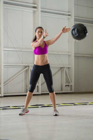 Young brunette woman exercising with a medicine ball in an indoor urban gym setting.の写真素材