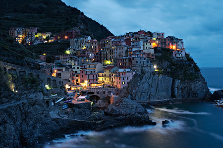 A picturesque coastal village with colorful old houses, illuminated, at dusk in Manarola, Italy.の写真素材