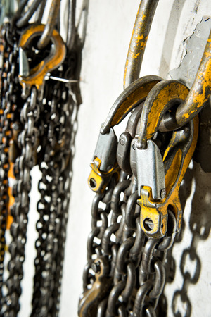 Several large industrial weathered yellow hooks attached to chain and a pulley.の写真素材
