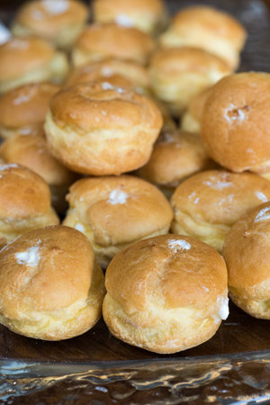 Looking at a glass plate filled with delicious decadent cream puffs.  Shot on a wood table.