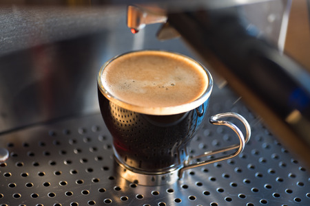 Modern glass cup of black coffee on a metal espresso machine.の写真素材
