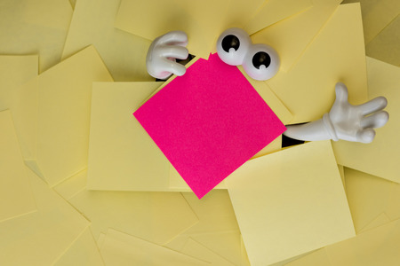 Hands reach out and eyes peer out from under several bright yellow sticky notes and a pink one as well.の写真素材